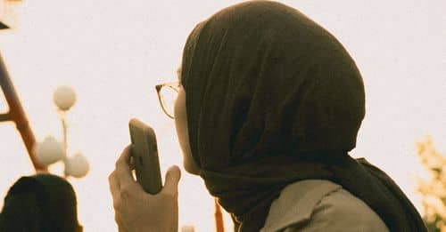 Young Woman in a Trench Coat and a Headscarf Talking on an iPhone