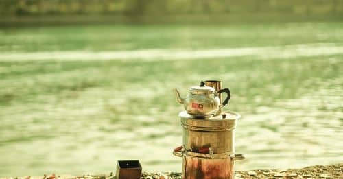 A jar of tea sits on the ground next to a lake