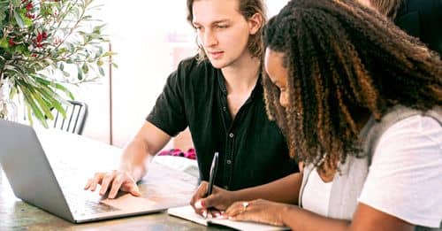 Man Working on Laptop while Woman Takes Notes