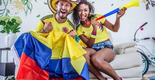 Excited ethnic couple with Colombian flag and toy pipe