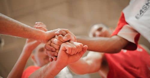 From below of crop multiethnic team of professional basketball players gathering and putting hands together while standing on playground before game