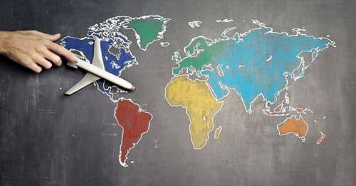 Top view of crop anonymous person holding toy airplane on colorful world map drawn on chalkboard