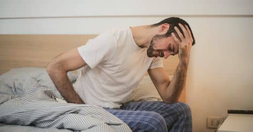 Young man in sleepwear suffering from headache in morning