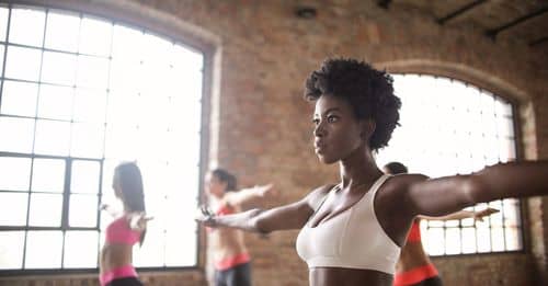 Confident fit ethnic woman training with other sportswomen in modern fitness studio