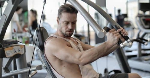 Side view of confident muscular man doing exercises on shoulder press machine while training in modern sports center