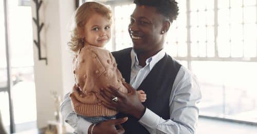 Cheerful young man holding little girl on hands in cafe