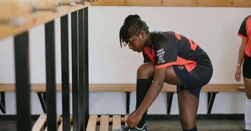 Side view of teenager wearing team sportswear and sneakers standing on benches and preparing for training in gym while looking away pensively