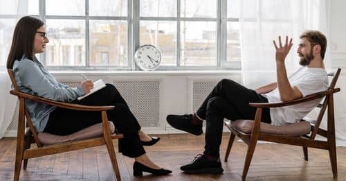 Person in Black Pants and Black Shoes Sitting on Brown Wooden Chair