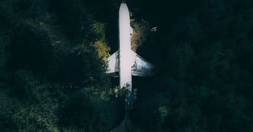 Drone view of modern white broken abandoned plane crashed in green dense forest