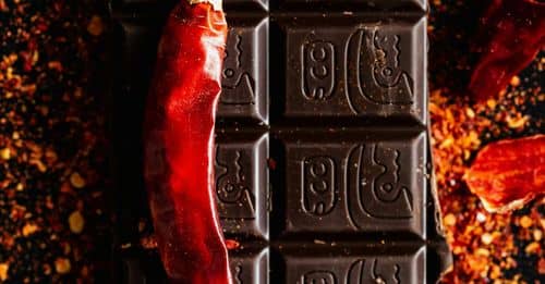 Top view of dry chili pepper placed on dark chocolate bar on dark table with ground spice