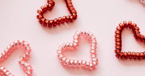 Colorful hair ties in shape of hearts on pink surface