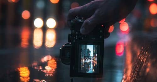 Person Holding Black Dslr Camera Taking Photo of City Lights during Night Time