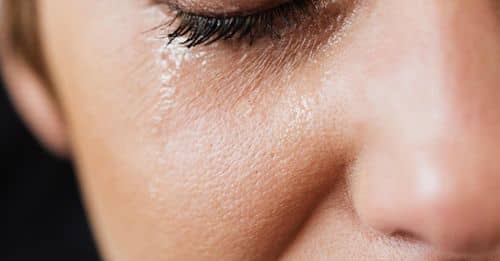 Closeup of crop sad adult lady with natural makeup having problems and crying alone