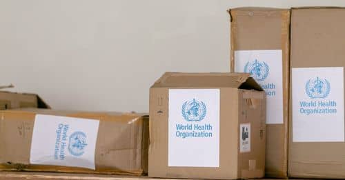 Blue emblem sticker of World Health Organization on carton boxes heaped on table