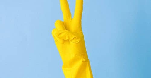 Crop hand of anonymous person in rubber gloves for cleaning demonstrating peace symbol against blue background