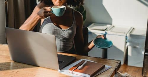 Black lady working remotely on netbook and drinking coffee