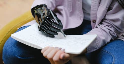 Woman with modern prosthesis of hand writing in notebook