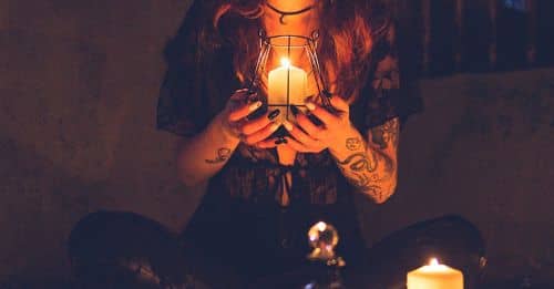 Spooky witch among candles during ritual