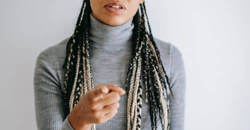 Ethnic female with long braids blaming  pointing with forefinger at camera standing against gray background