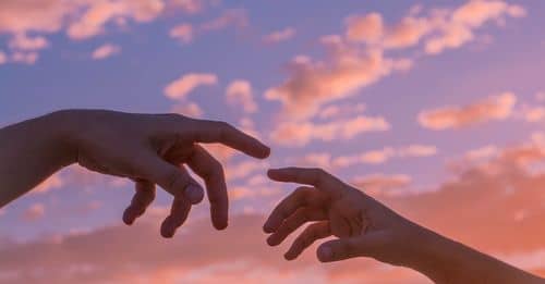 Crop anonymous people pulling hands to each other against bright sunset sky with clouds