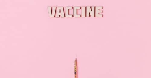 Vaccine Text and A Person Wearing Latex Glove While Holding a Syringe on Pink Background