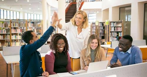 Cheerful multiethnic students having high five with teacher