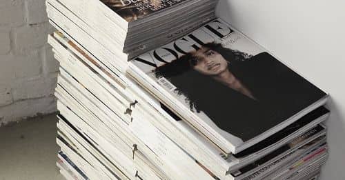 High angle many fashion magazines stacked on floor against white brick wall in studio