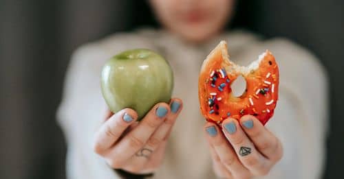 Woman showing apple and bitten doughnut