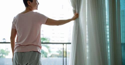 Happy Asian woman with short hair opening curtains of window