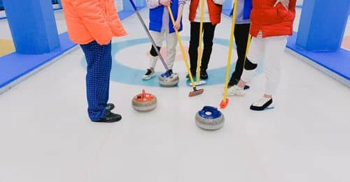 Crop players of curling professional team in sportswear with brooms and stones standing on ice rink