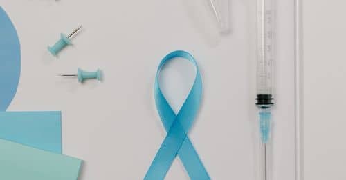 A Blue Ribbon Symbol for Prostate Cancer Beside a Syringe on White Surface