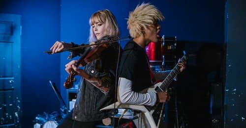 Man in Black Shirt Playing Electric Guitar Beside Woman in Black Jacket Playing Violin