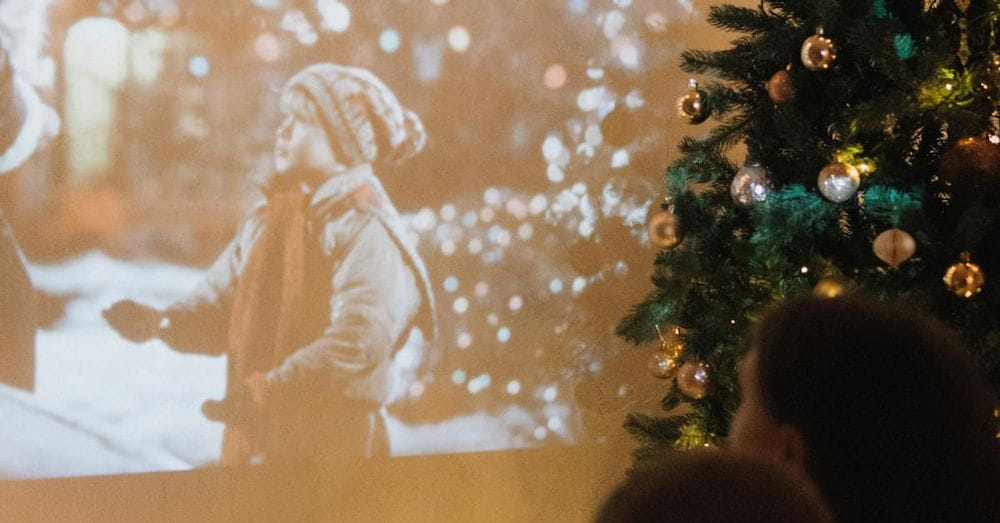 A Couple Watching a Movie Displayed on a Wall from a Projector next to a Christmas Tree