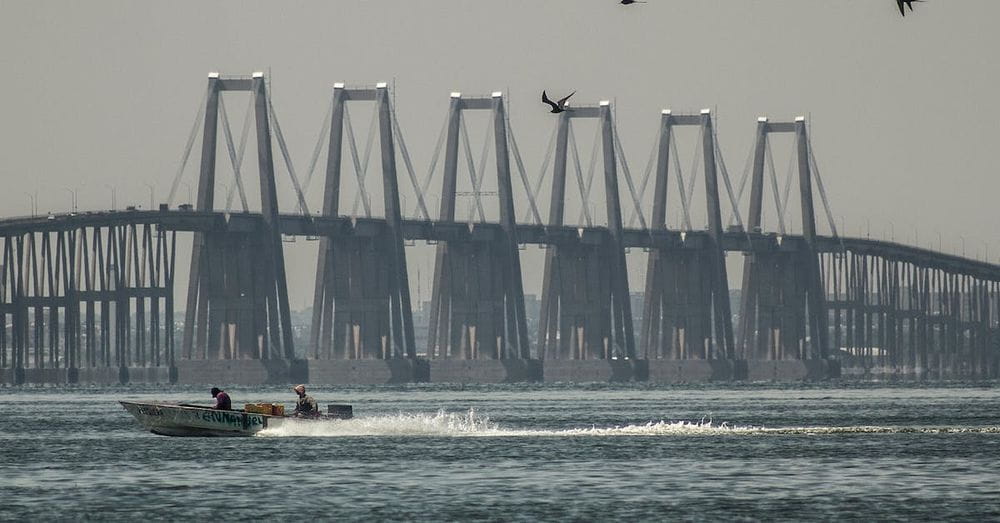 A boat is traveling across the water near a bridge