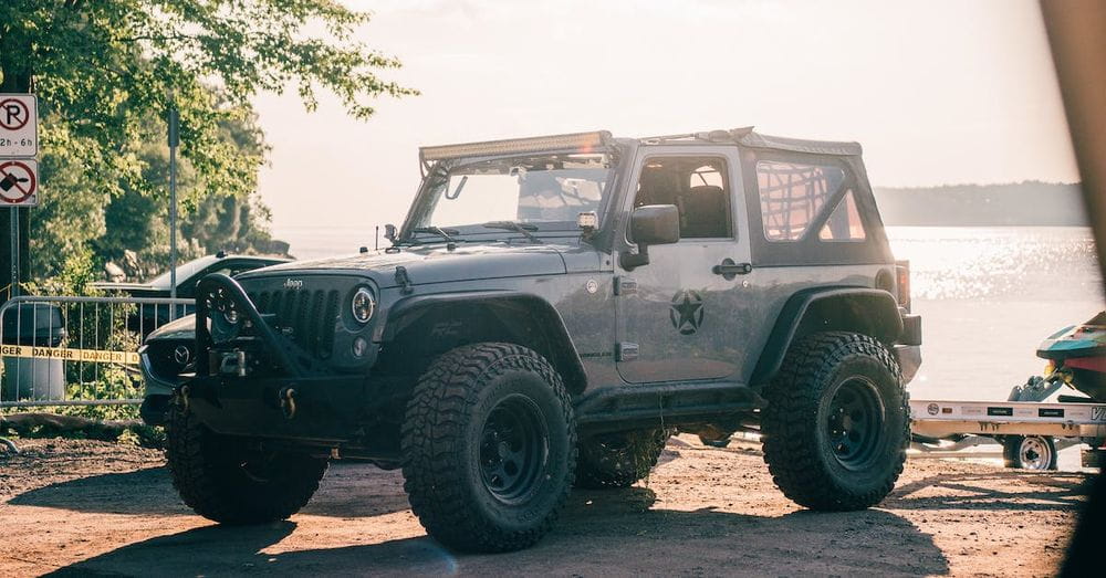 A jeep parked on the beach near a lake