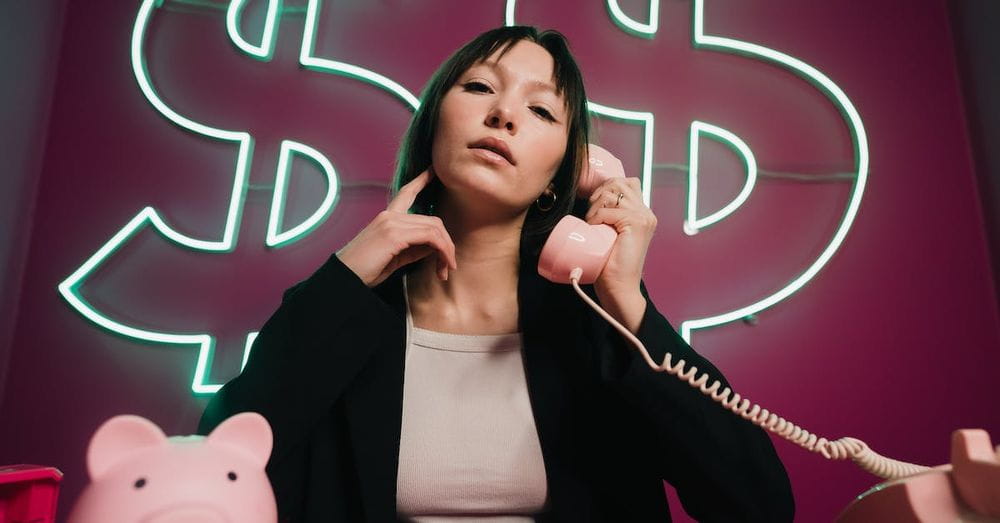 A woman sitting at a desk with a pink piggy bank and a sign that says dollar