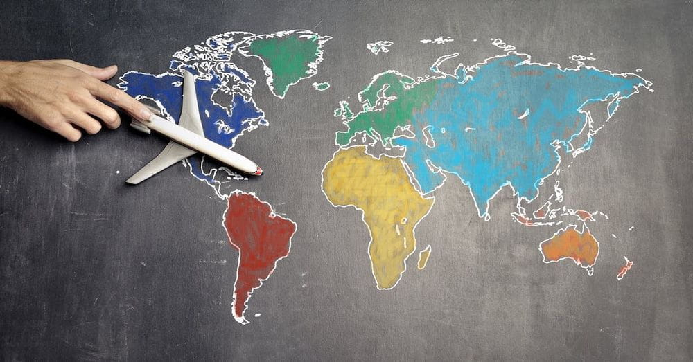 Top view of crop anonymous person holding toy airplane on colorful world map drawn on chalkboard