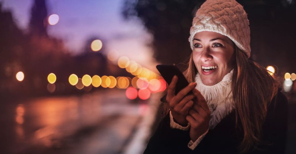 Cheerful woman recording voice message on smartphone in street