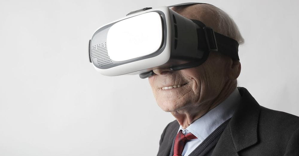 Smiling elderly gentleman wearing classy suit experiencing virtual reality while using modern headset on white background