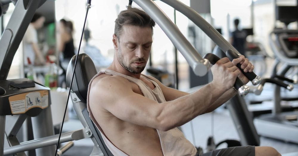 Side view of confident muscular man doing exercises on shoulder press machine while training in modern sports center