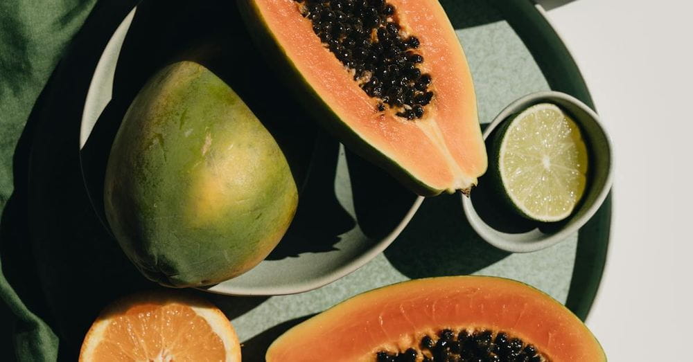 Top view of halves of ripe papaya together with oranges and limes placed on green round dishes and green fabric on white background