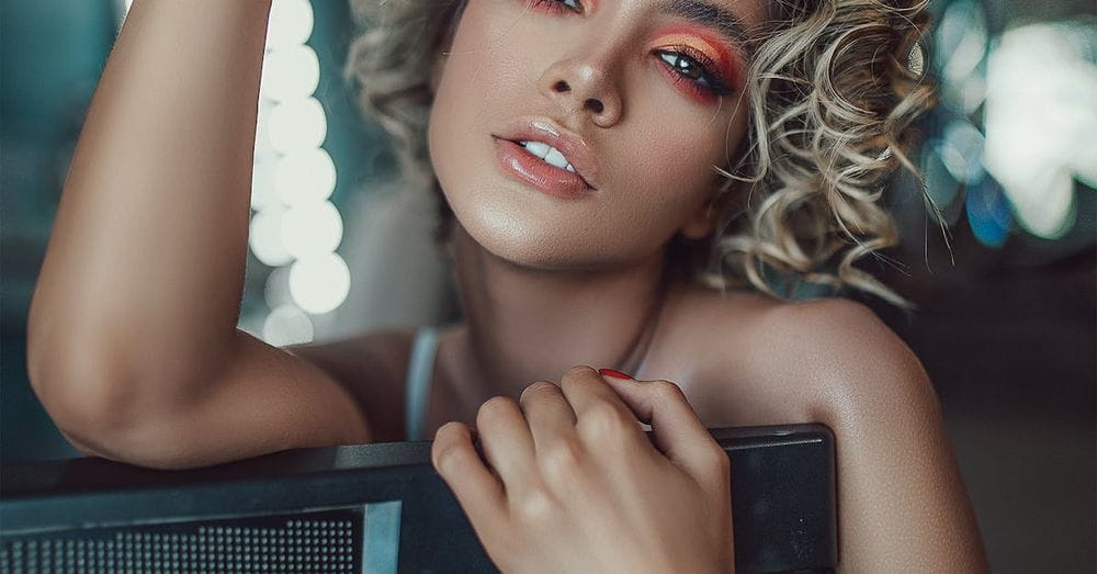 Self assured young female singer with curly hair and makeup standing in modern studio with synthesizer before concert