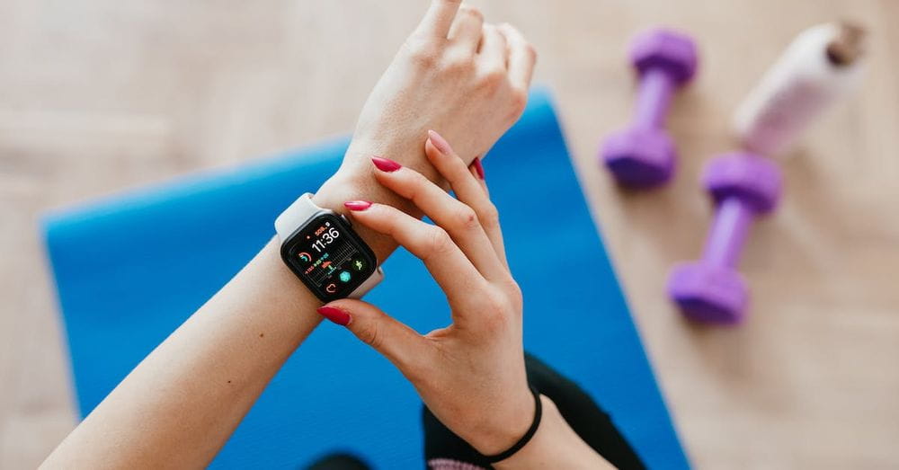 Anonymous sportswoman checking smart watch and sitting on mat