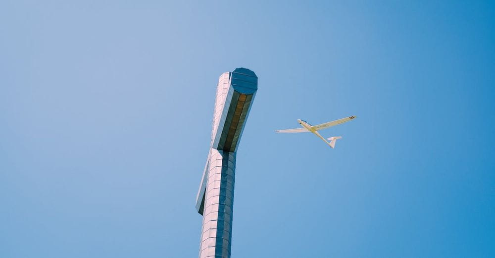 From below of high metal Nivolet Cross with plane flying over cloudless blue sky in France