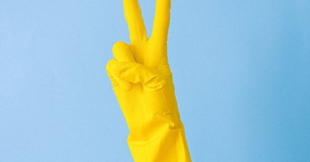 Crop hand of anonymous person in rubber gloves for cleaning demonstrating peace symbol against blue background