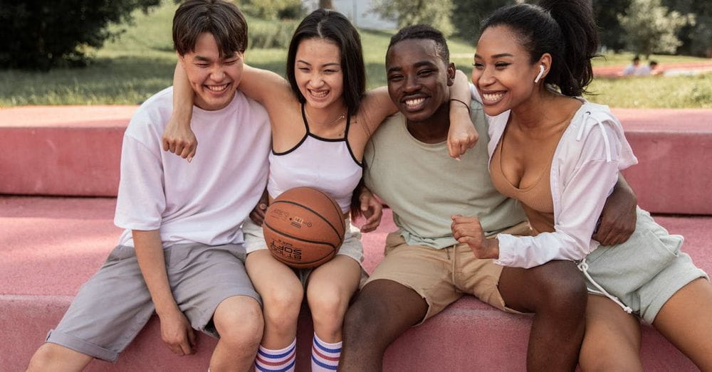 Happy multiracial friends embracing on bench after basketball training