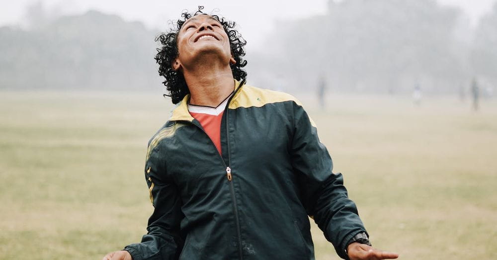 Smiling football male player with curly hair wearing sportswear hitting soccer ball with head while playing on field