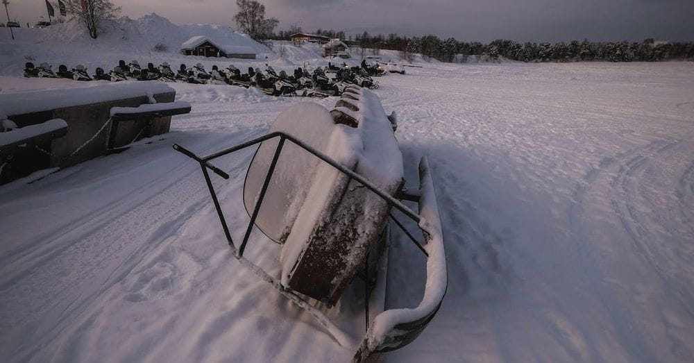 Forgotten snowmobile covered with hoarfrost and placed on side on snow in winter time  in field against cloudy sky