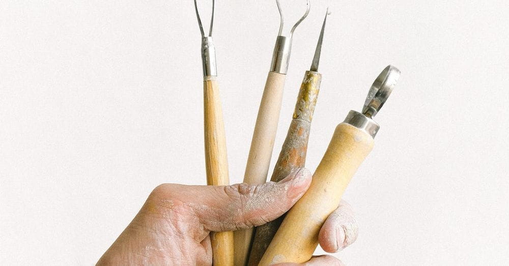 Anonymous male master with set of instrument for clay modeling in dirty hand standing on white background in professional workshop