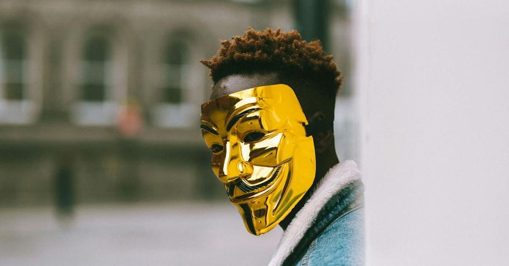 Black activist in golden Anonymous mask standing on city street